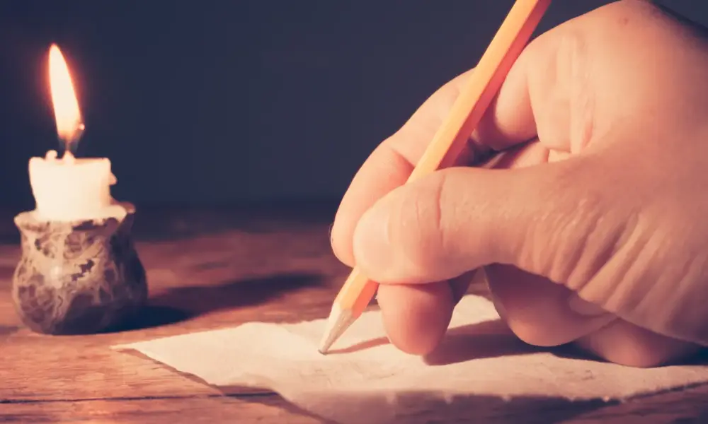 Autor werden – Hand schreibt mit Bleistift bei Kerzenlicht