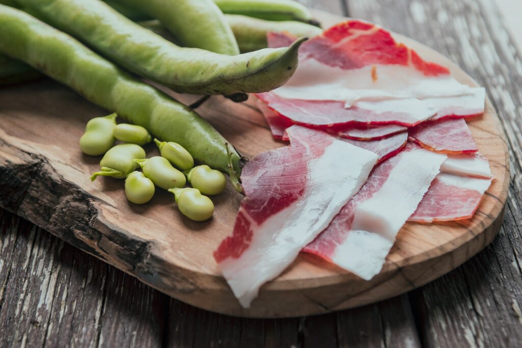 Frühlingspicknick in der Toskana mit frischen Favabohnen und Prosciutto auf Holzbrett