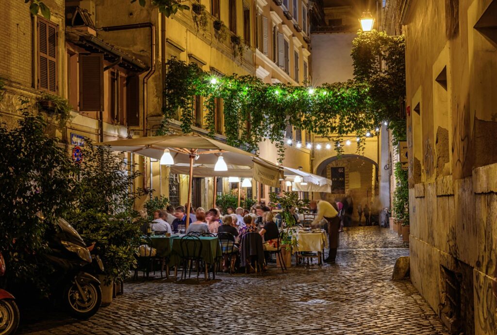 Belebtes italienisches Restaurant in einer Altstadtgasse am Abend als Sinnbild für das echte Leben in Italien