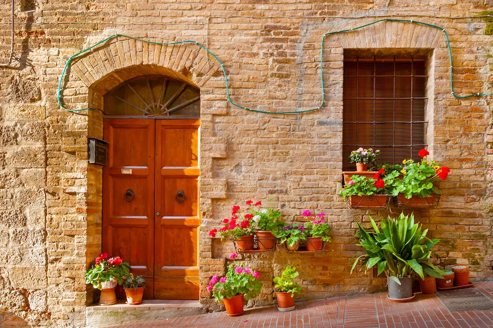 Immobilie in Italien – traditionelle Haustür mit Blumen an einer historischen Backsteinfassade