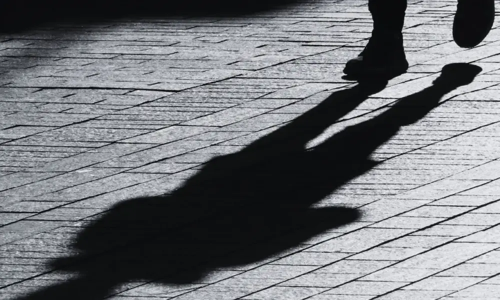 Pseudonym – gehende Person mit langem Schatten auf Kopfsteinpflaster