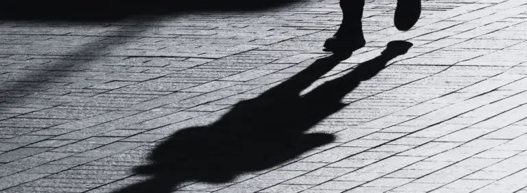 Pseudonym – gehende Person mit langem Schatten auf Kopfsteinpflaster
