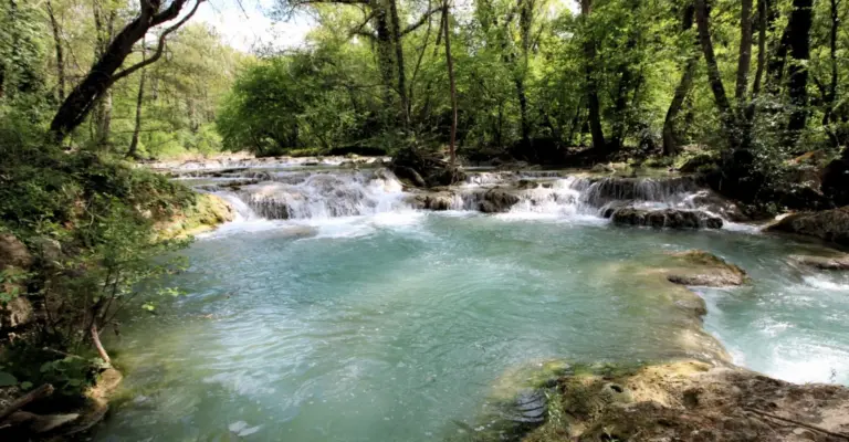 Toskana Wochenschau – türkisblauer Fluss mit kleinen Wasserfällen in einem bewaldeten Gebiet