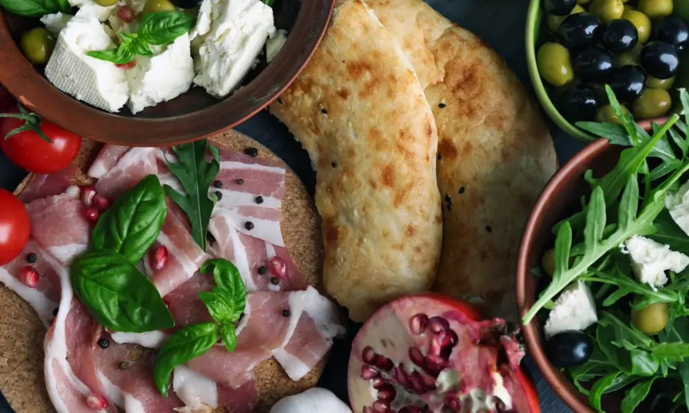 Mediterrane Küche – Auswahl mediterraner Speisen mit Fladenbrot, Oliven, Schinken, Käse, Salat und Basilikum