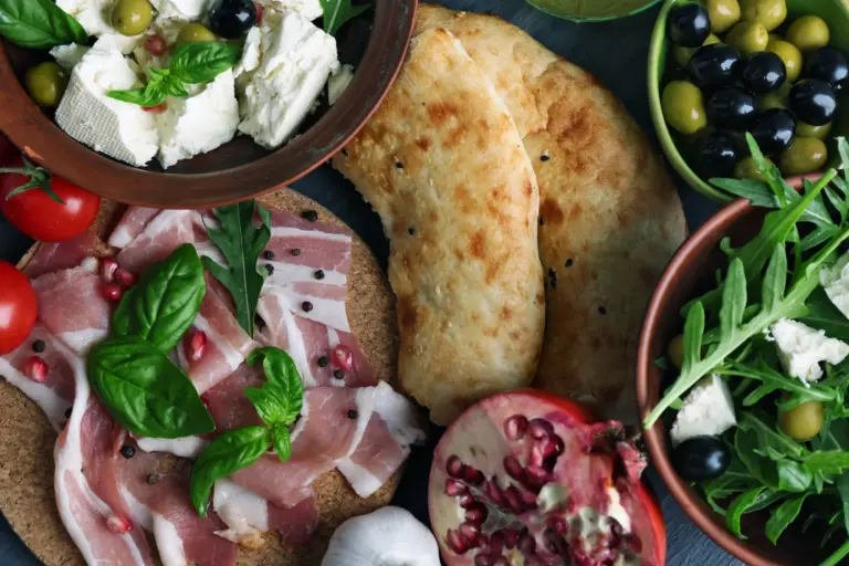 Mediterrane Küche – Auswahl mediterraner Speisen mit Fladenbrot, Oliven, Schinken, Käse, Salat und Basilikum
